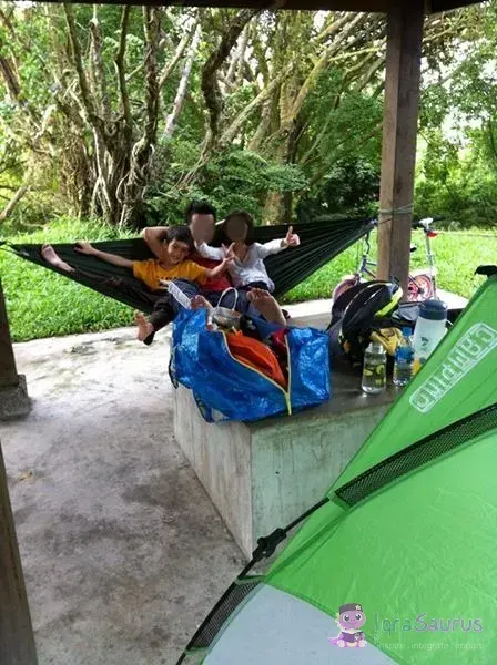 Children in a hammock under a shelter, with a green tent beside them