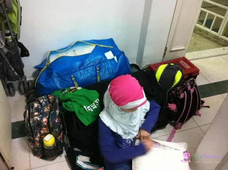 A child sitting among packed bags by the front door