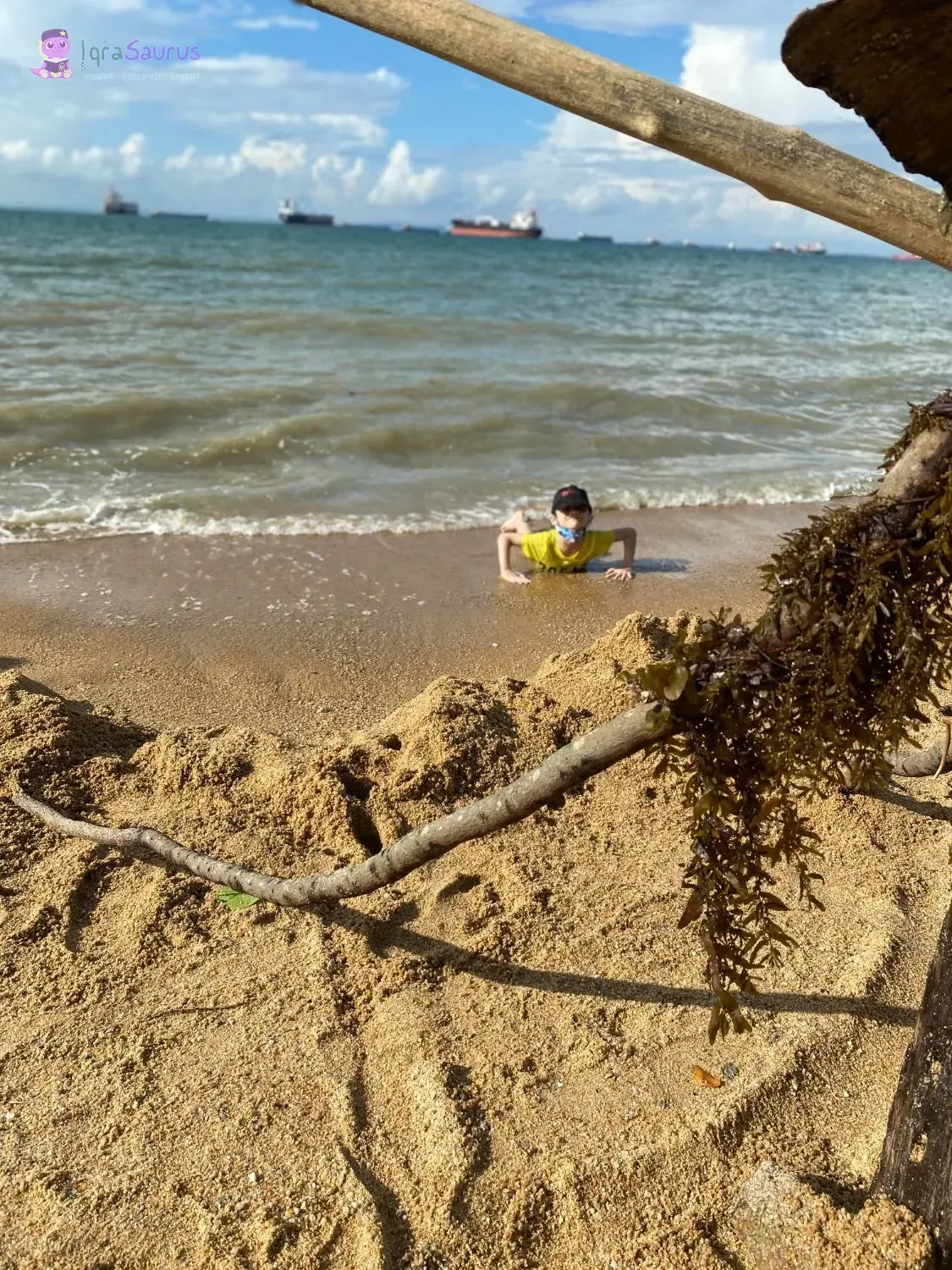 A boy in a face mask doing push-ups at the water's edge, with ships at anchor out at sea