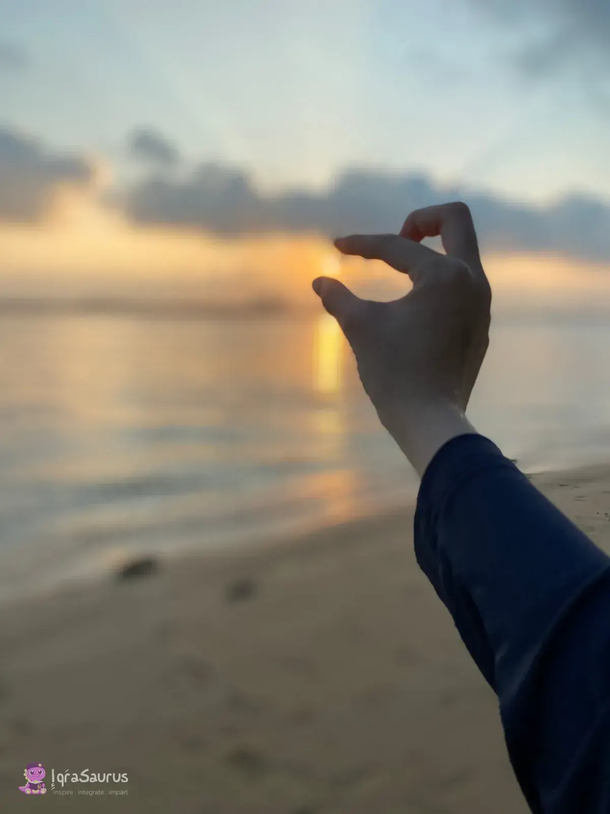 A hand pretending to pinch the setting sun over the sea